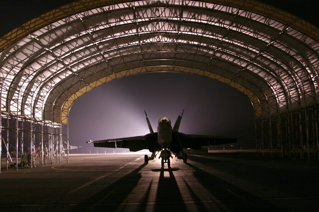 hangar-jet-aircraft-fighter-72593-72593 Silhouetted fighter jet in an illuminated hangar at night creates a dramatic scene.